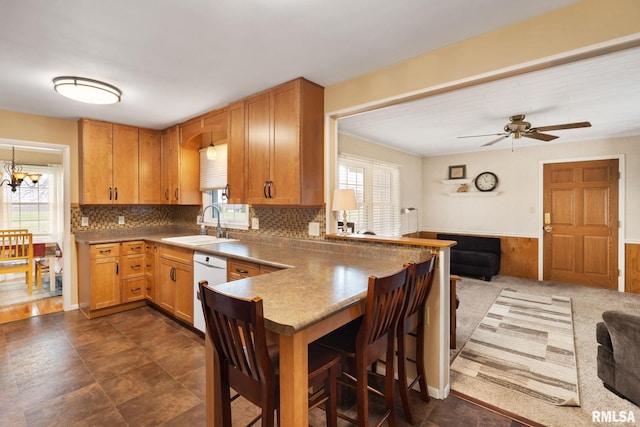 kitchen featuring a peninsula, dishwasher, a sink, a breakfast bar, and backsplash