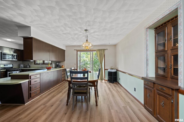 dining area with wallpapered walls, light wood-type flooring, a textured ceiling, and baseboards