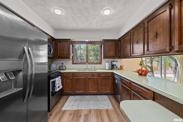 kitchen featuring appliances with stainless steel finishes, light countertops, light wood finished floors, a sink, and decorative backsplash