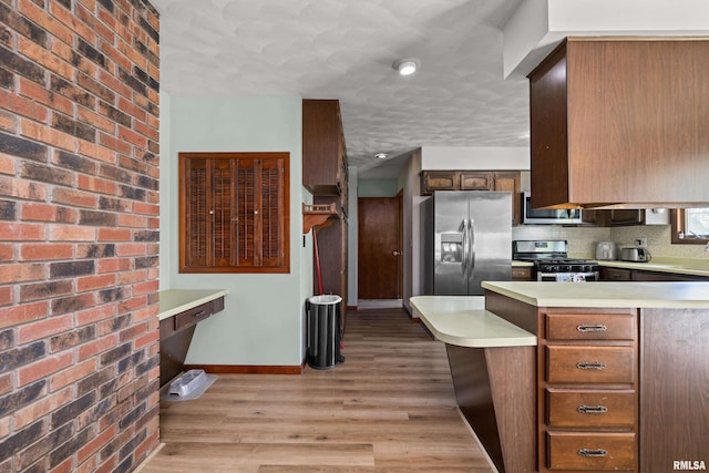 kitchen with appliances with stainless steel finishes, light countertops, baseboards, a peninsula, and light wood-type flooring