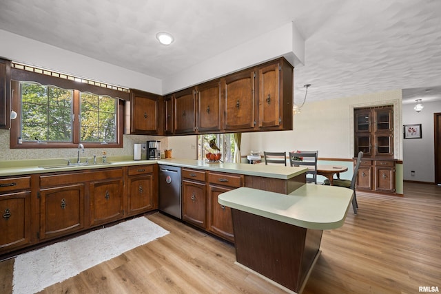 kitchen with stainless steel dishwasher, a sink, a peninsula, light countertops, and light wood-type flooring