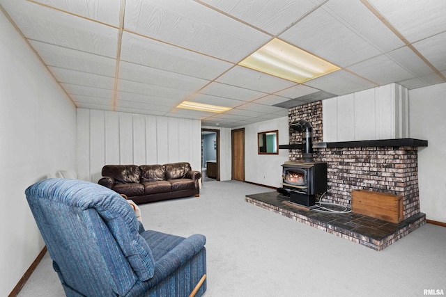 living room with carpet flooring, a wood stove, baseboards, and a paneled ceiling