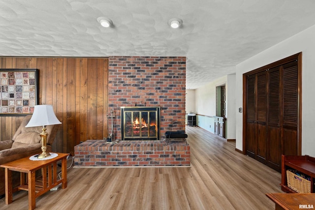living area featuring wood finished floors, a fireplace, a textured ceiling, and wooden walls