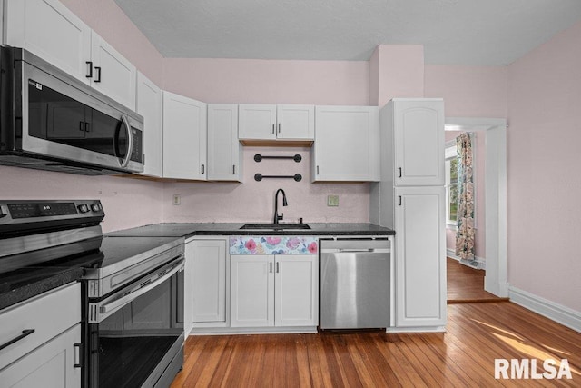 2350 Jefferson Ave, Davenport, IA 52803 - kitchen featuring stainless steel appliances, a sink, dark countertops, wood finished floors, and white cabinets