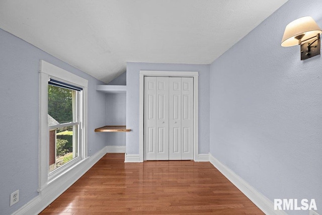 2350 Jefferson Ave, Davenport, IA 52803 - unfurnished bedroom with wood finished floors, baseboards, vaulted ceiling, a textured wall, and a closet