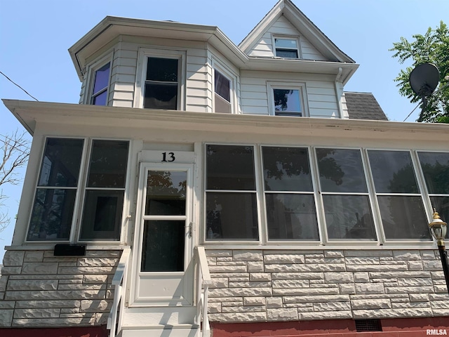 view of front of house with a sunroom, stone siding, and entry steps