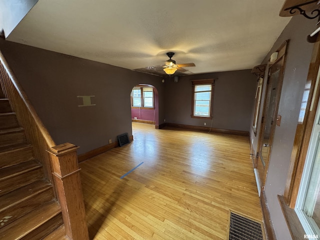 empty room featuring arched walkways, light wood-style flooring, a ceiling fan, and stairs