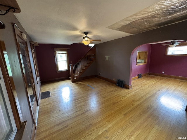 unfurnished living room featuring ceiling fan, light wood-type flooring, arched walkways, stairs, and baseboards