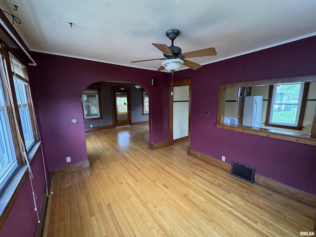 spare room featuring arched walkways, hardwood / wood-style flooring, baseboards, a ceiling fan, and crown molding