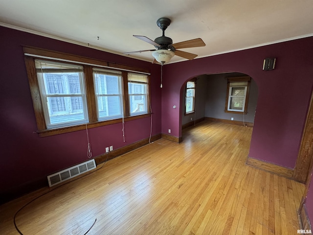 unfurnished room featuring arched walkways, baseboards, light wood finished floors, crown molding, and a ceiling fan