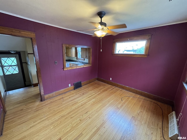 spare room featuring light wood finished floors, a ceiling fan, ornamental molding, and baseboards