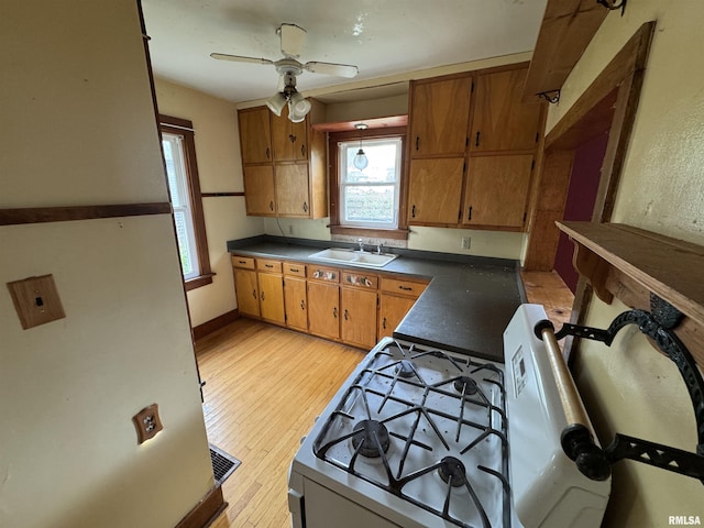 kitchen featuring brown cabinets, a sink, light wood-type flooring, ceiling fan, and dark countertops