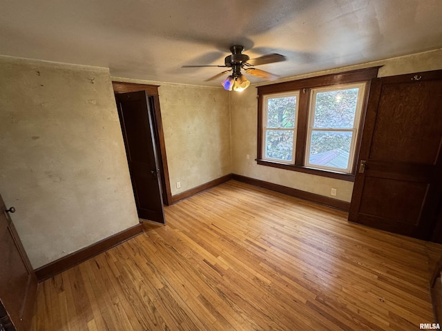spare room featuring light wood finished floors, a ceiling fan, and baseboards