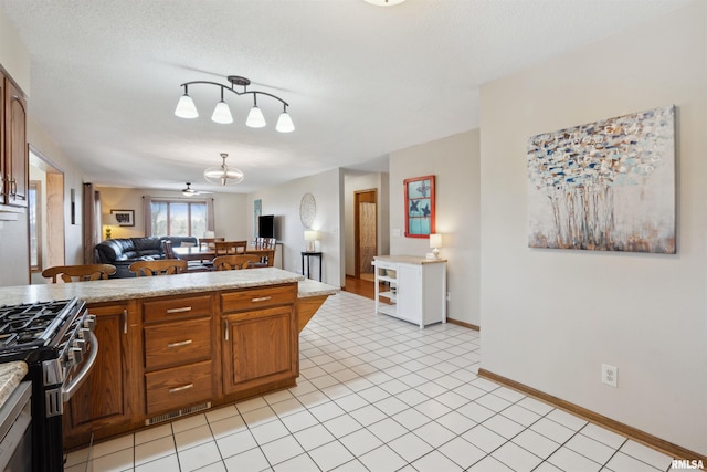 kitchen with light countertops, open floor plan, brown cabinets, stainless steel gas range, and baseboards