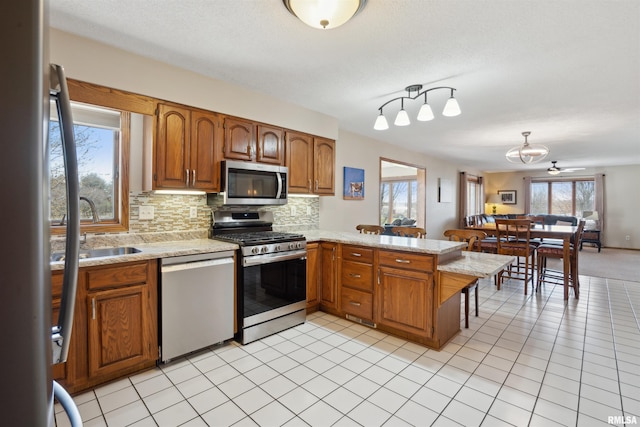 kitchen featuring appliances with stainless steel finishes, light countertops, a peninsula, decorative backsplash, and brown cabinets