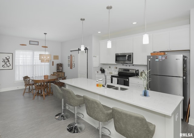 6811 Genesis Way, Bettendorf, IA 52722 - kitchen featuring appliances with stainless steel finishes, white cabinets, light wood-type flooring, a barn door, and a kitchen bar