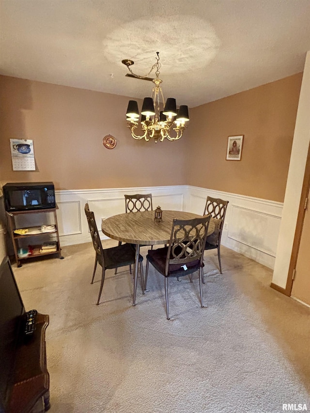 dining room featuring a chandelier, carpet, wainscoting, and a decorative wall