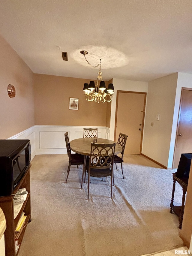 dining space with light colored carpet, a chandelier, a wainscoted wall, and a textured ceiling