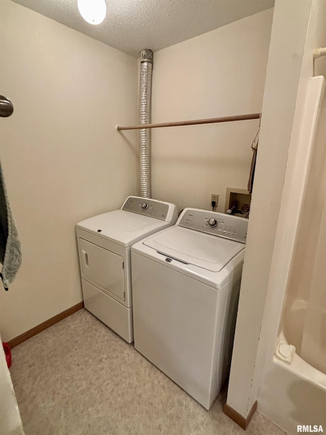 clothes washing area with washer and clothes dryer, light carpet, a textured ceiling, and baseboards