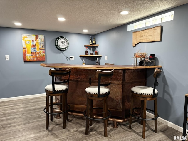indoor wet bar with a textured ceiling, wood finished floors, recessed lighting, and baseboards