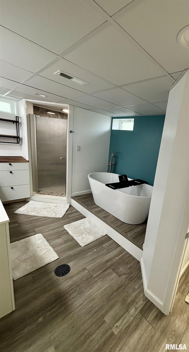 bathroom featuring a shower stall, baseboards, a paneled ceiling, a soaking tub, and wood finished floors