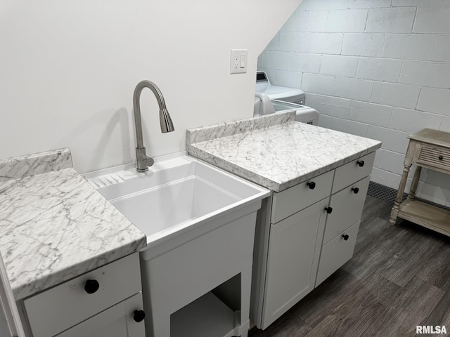 clothes washing area with a sink, dark wood-style flooring, concrete block wall, and washing machine and clothes dryer