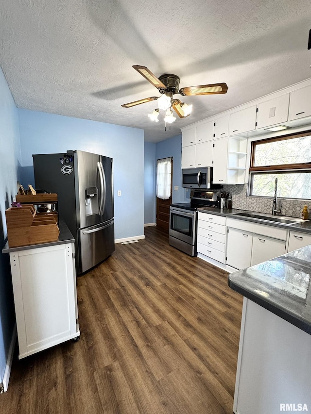 kitchen featuring appliances with stainless steel finishes, a sink, dark countertops, and a textured ceiling