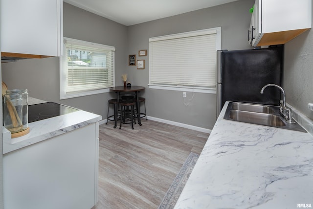 kitchen featuring a sink, freestanding refrigerator, light wood finished floors, white cabinetry, and baseboards