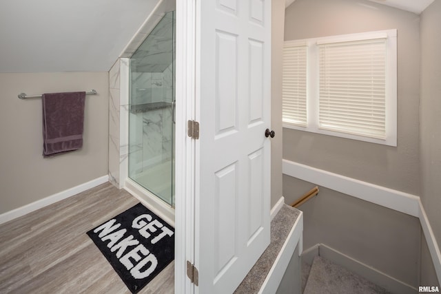 bathroom featuring a marble finish shower, vaulted ceiling, wood finished floors, and baseboards