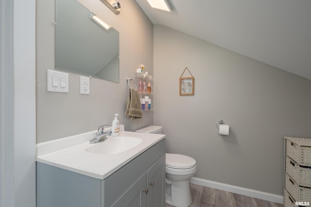 bathroom with toilet, vanity, wood finished floors, vaulted ceiling, and baseboards