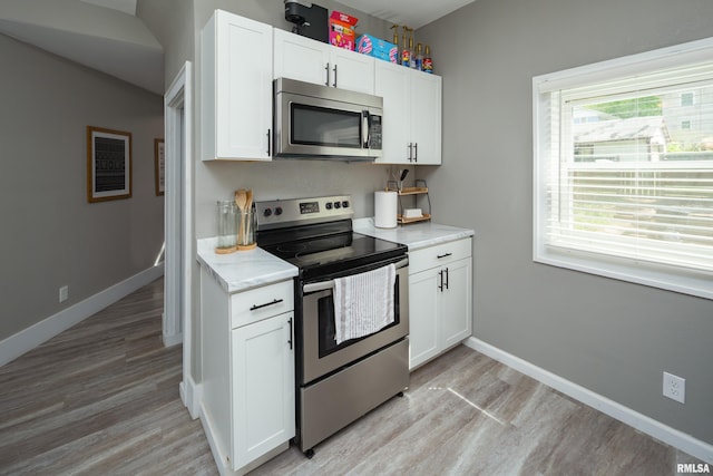 kitchen with appliances with stainless steel finishes, light wood-type flooring, white cabinetry, and baseboards