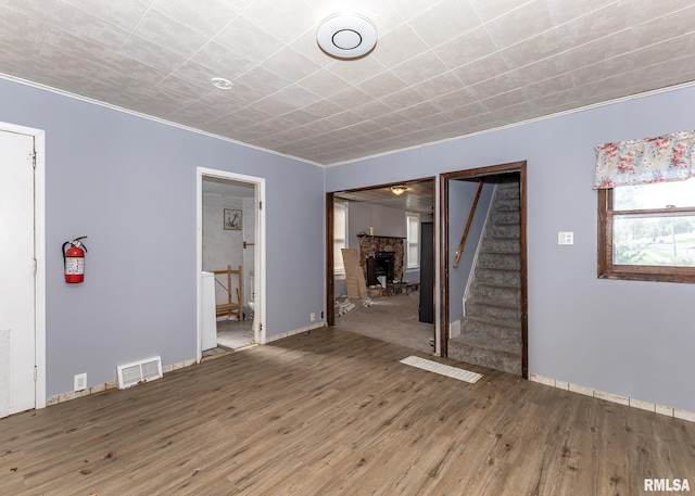 unfurnished living room with stairway, wood finished floors, ornamental molding, and baseboards