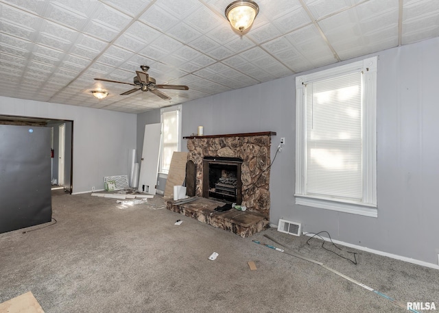 unfurnished living room with ceiling fan, carpet flooring, baseboards, and a stone fireplace
