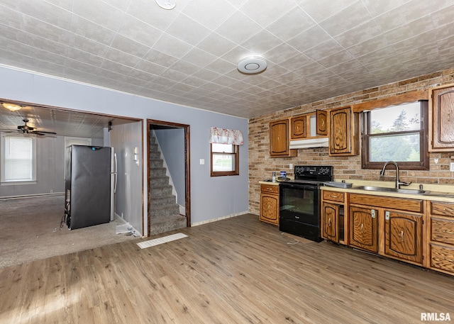 kitchen with black range with electric stovetop, a sink, freestanding refrigerator, under cabinet range hood, and brown cabinetry