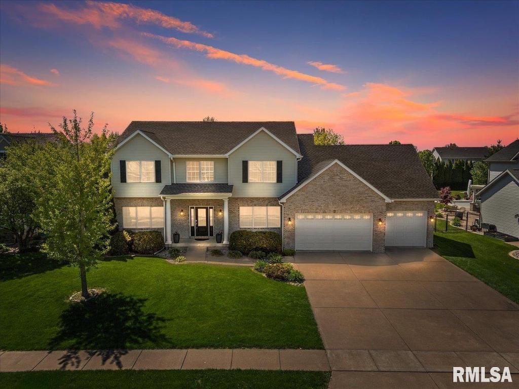traditional home featuring a garage, concrete driveway, a yard, and brick siding