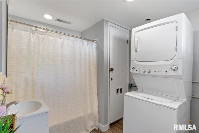 clothes washing area featuring stacked washing machine and dryer and wood finished floors