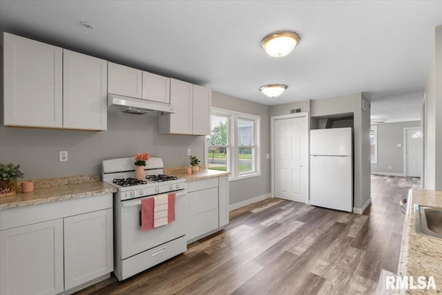 kitchen featuring white appliances, under cabinet range hood, wood finished floors, white cabinets, and a sink