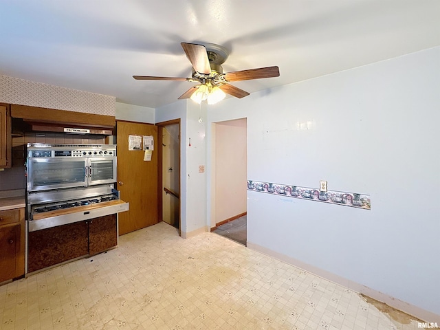 kitchen featuring wall oven, light flooring, a ceiling fan, brown cabinets, and light countertops