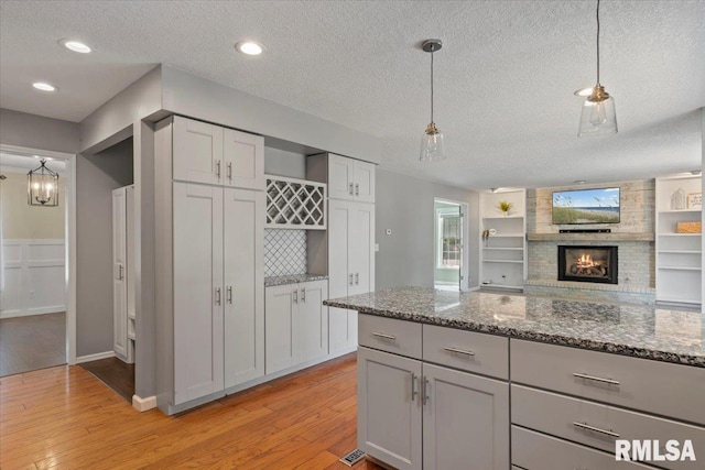 4690 Lindbergh Dr, Bettendorf, IA 52722 - kitchen featuring a textured ceiling, light wood-style flooring, a fireplace, stone countertops, and hanging light fixtures
