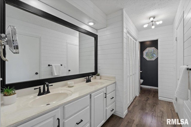 4690 Lindbergh Dr, Bettendorf, IA 52722 - full bath with wood finished floors, double vanity, toilet, a textured ceiling, and wood walls