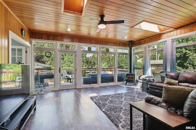 sunroom / solarium featuring a skylight, a wood stove, healthy amount of natural light, wood ceiling, and wood walls