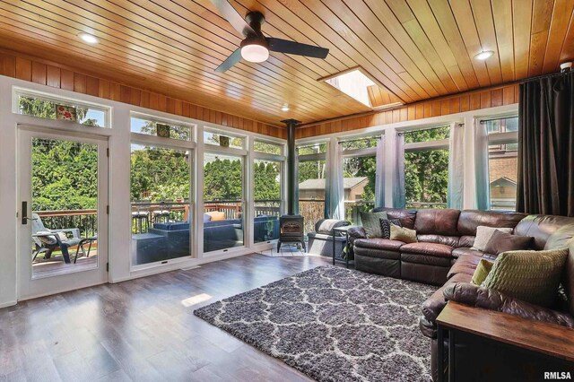 sunroom featuring a wood stove, wood ceiling, plenty of natural light, a skylight, and wood finished floors