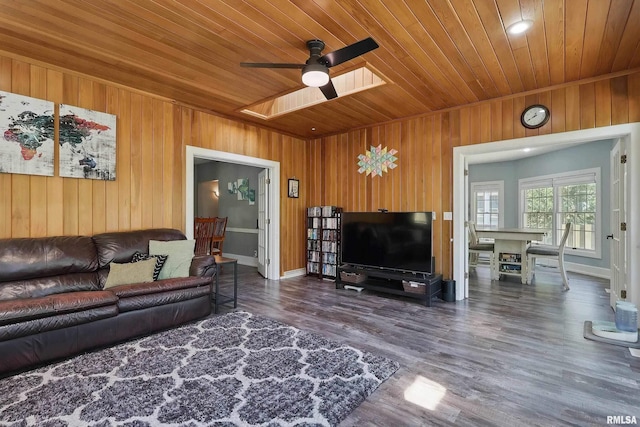 living room with wooden ceiling, wooden walls, ceiling fan, wood finished floors, and baseboards