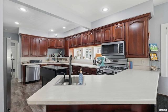 kitchen featuring appliances with stainless steel finishes, a peninsula, a sink, tasteful backsplash, and dark wood-style floors