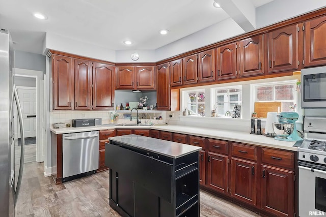 kitchen with stainless steel appliances, a sink, decorative backsplash, light wood-style flooring, and a center island