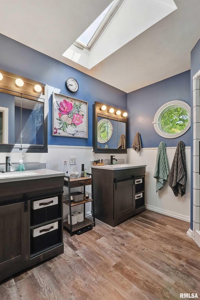 full bathroom featuring a skylight, wood finished floors, and two vanities