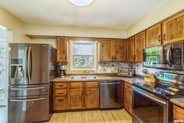 1960 Tam-O-Shanter Dr, Bettendorf, IA 52722 - kitchen featuring stainless steel appliances, a sink, brown cabinets, light wood-style flooring, and backsplash