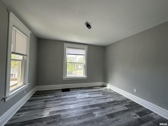 empty room featuring plenty of natural light, baseboards, and dark wood-style floors