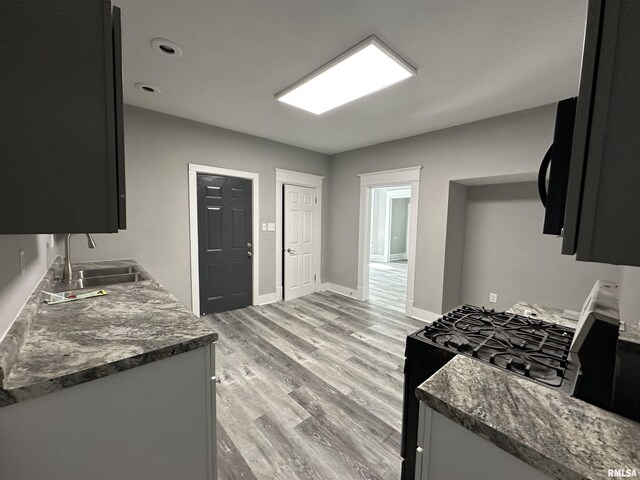 kitchen featuring a sink, black appliances, light wood-style floors, and baseboards
