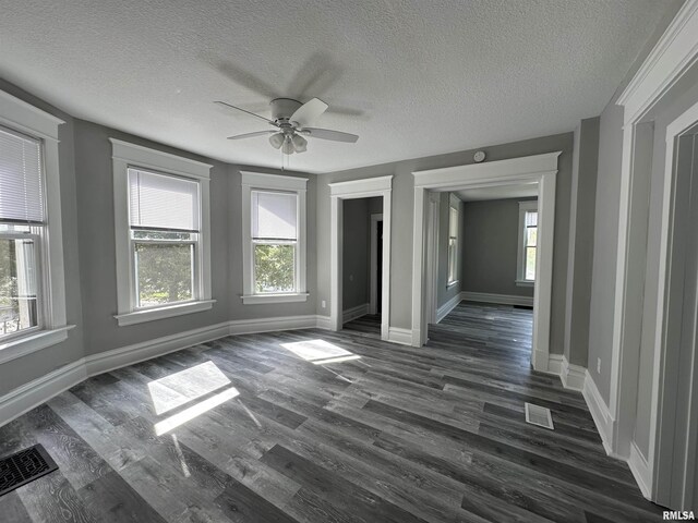spare room with healthy amount of natural light, a textured ceiling, ceiling fan, dark wood finished floors, and baseboards